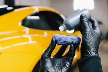Process of pouring ceramic liquid from bottle on sponge to apply a protective nano layer on car. Detailing service worker applies ceramic protective liquid on sponge close-up.