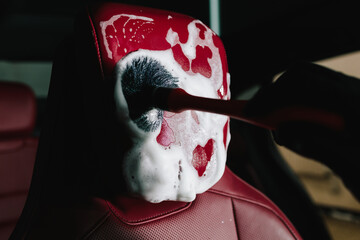 Meticulous car interior detailing using brush with foam solution and brush. Washing red leather car...