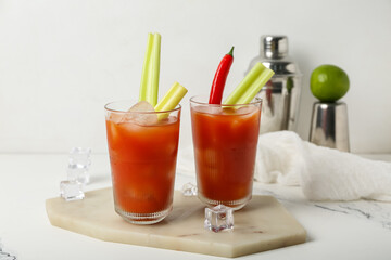 Glasses of bloody mary cocktail with chili pepper, celery and ice cubes on white background
