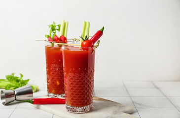 Glasses of bloody mary cocktail with chili peppers and celery on white tile table