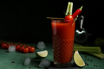 Glass of bloody mary cocktail with chili pepper, celery and lime on green table