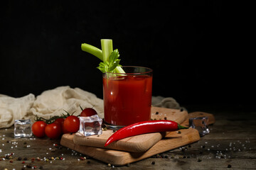 Glass of bloody mary cocktail with celery, chili pepper and peppercorns on wooden table