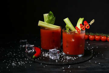 Glasses of bloody mary cocktail with celery and chili pepper on black background