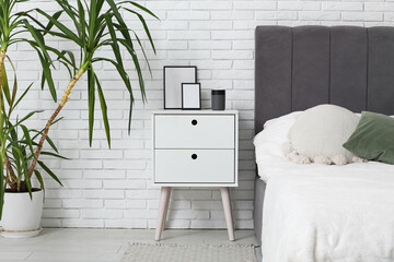 Air humidifier with frames on table near white brick wall in bedroom