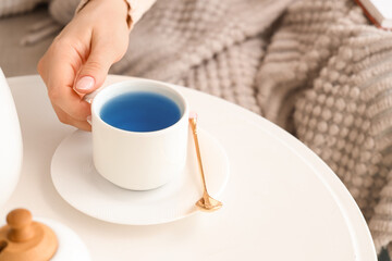 Woman taking cup of tasty blue tea at home. Closeup