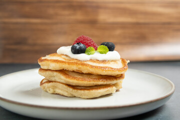 Stack of golden pancakes topped with whipped cream, fresh blueberries, raspberries, and mint leaves. A perfect breakfast or brunch dish with a delicious and appetizing look