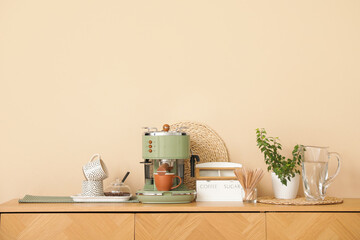 Modern coffee machine with cups, houseplant and bowl of beans on counter in kitchen