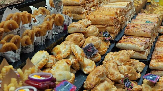 Close-up shot of a market food stall displaying golden empanadas, crispy churros, and delicious baked goods at Mercat de la Boqueria in Barcelona. A vibrant scene of Spanish street food.