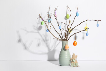 Vase of tree branches with colorful Easter eggs and toy bunny on white background