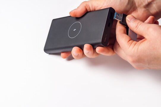 Hands connecting a USB cable to a black power bank with wireless charging function on a white surface.