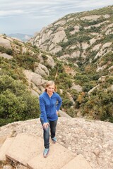 Fototapeta premium Portrait of young woman posing in mountains on vacation trip. Adult woman walking and enjoying the view of the mountains on cloudy day. Adult female feels freedom on top of mountain. Travel concept
