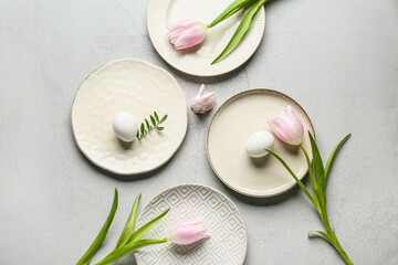 Different clean plates with Easter eggs, toy bunny and beautiful tulip flowers on grey background