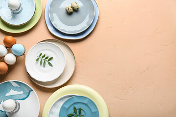 Different clean plates with Easter eggs and fresh green leaves on beige background