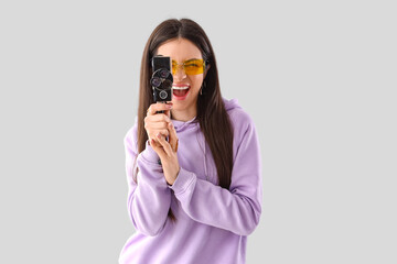 Stylish young woman in lilac hoodie with retro camera on light background