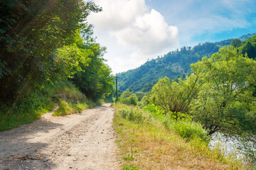 rural landscape with road in summer. countryside nature with mountain in background. rustic scenery with green grass on hill and blue sky. scenic view of gravel ground street in valley