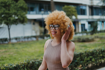 Fashionable woman with a distinctive afro hairstyle and eyeglasses is listening to music with...