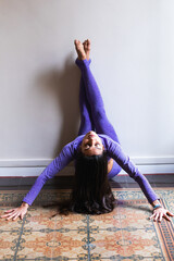 Active woman doing yoga, executing a modified shoulder stand with legs supported by a wall