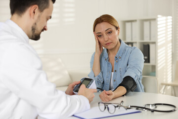 Fototapeta premium Cardiologist measuring patient's blood pressure at table in hospital
