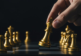 Hand moving a golden chess king piece on a chessboard against a dark background in a studio shot