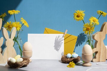 White empty envelope Postcard copy space traditional greeting card to christian holiday. Festive mood composition with bunnies eggs and yellow flowers on pastel blue background. Sustainable natural