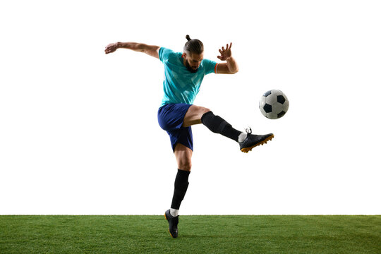 Young sporty man, dressed blue uniform, leaping and kicking ball in motion against white background on grassy playground. Concept of professional sport, championship, match, victory.