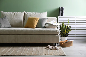 Comfortable sofa with pillows and houseplant near green wall indoors
