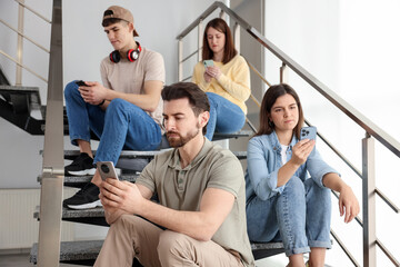 Fototapeta premium Internet addiction. Group of people with smartphones on stairs indoors