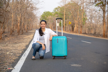 Happy Indian solo traveler with her stroller or bag waiting roadside
