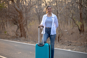 Happy Indian solo traveler with her stroller or bag waiting roadside
