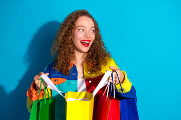 Smiling woman showcasing colorful shopping bags against vibrant blue background, radiating joy and...