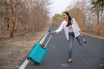 Happy Indian solo traveler with her stroller or bag waiting roadside
