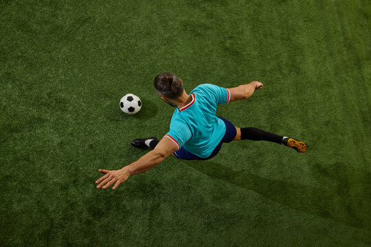 Top-down perspective of skilled football player executing powerful pass, leg fully extended, ball rolling on stadium grass. Concept of game control, strategy, professional sport, match, playmaking.