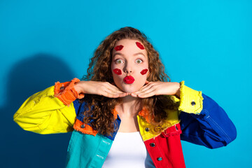 Cheerful Young Woman in Colorful Jacket Showing Playful Lipstick Mark Gesture on Blue Background
