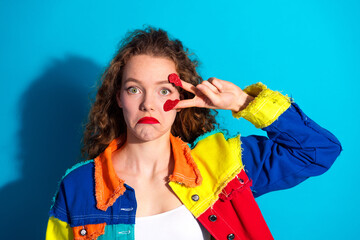 Smiling young woman in vibrant colorful outfit against a bright blue background expressing humor...