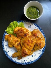 Cooked chicken and green sauce presented on decorative white plate