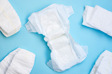 Many white diapers on light blue table background. Top view.