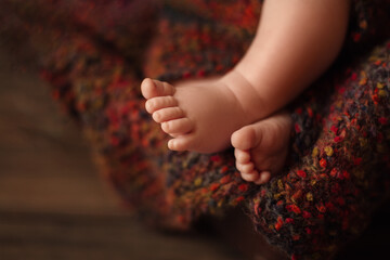 Baby Feet close up on woolen brown Blanket. Newborn Toes Closeup over Brown dark background. Sleeping Baby Tiny Foot. Infant Health Skin Care and Childcare Concept