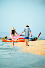 Obraz premium Couple traveler holding hand walking together at the edge of the sea beach, summertime traveling together enjoyment