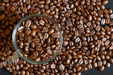 Overhead shot of a glass mug brimming with roasted coffee beans against a scattered background, perfect for coffee-themed ads, menus, or packaging. Photo