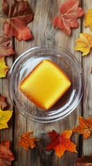 Top view of lemon sponge cake in transparent plate on a brown rustic wooden planks surrounded by autumn leaves, hyper realistic photo with high quality