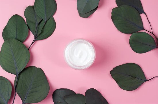 Jar of cosmetic cream with eucalyptus on pink. Flat lay. Rotating background. 