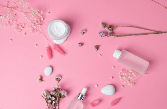 Cosmetic skin care products with flowers on pink. Flat lay. Rotating background. 
