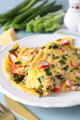 Omelet with crab sticks, cheese and green onions on white plate on blue background
