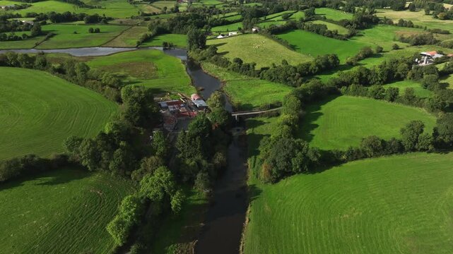 Finn River, County Monaghan, Ireland, September 2022. Drone pushes forwards towards a river flowing through lush green fields along the Irish border with Northern Ireland.