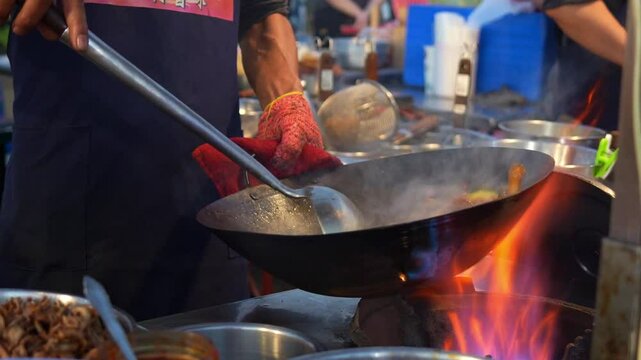 A street food vendor expertly stirs a wok over roaring flames, tosses ingredients in the wok and creating a savory stir-fry dish.