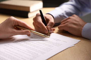 Woman pointing at document and man putting signature at wooden table, closeup