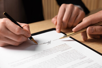 Man pointing at document and woman putting signature at table, closeup