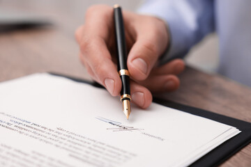 Fototapeta premium Man putting signature on document at table, closeup