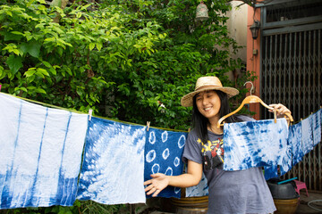 Thai women tie batik dyeing handkerchief indigo color and hanging process dry clothes in the sun at...