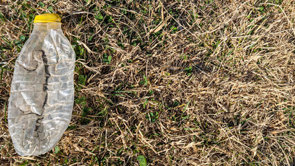 Discarded yellow capped plastic bottle lying crumpled on withered grassland, representing environmental degradation and waste impact on natural landscapes